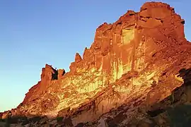 Rainbow Valley's main sandstone formation, a steep and wide bluff, glowing red, orange and yellow in the light of the setting sun