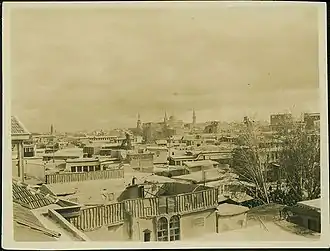 Monochrome city skyline, with roofs and trees visible.