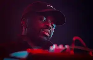 close-up of Alfa Mist wearing a ball cap, looking down at a DJ mixer