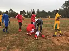 an injured player lies in the grass while several teenaged players look on