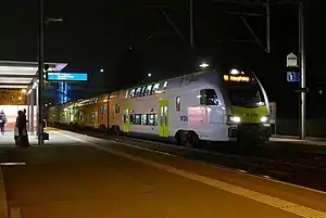 Green-and-white train at station with canopy-covered platform
