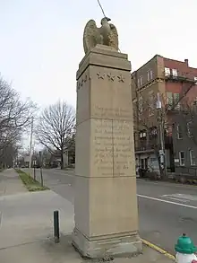 View up at an Eagle sculpted in stone on top of a square monolith with an inscription about Marietta's establishment.