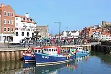 Three small brightly-painted boats in a harbour, with a church on the hill behind.