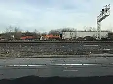 Two locomotives parked next to a building, with more tracks in the foreground along with a signal gantry.