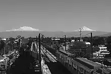 A picture of Line 12's overground track with a train passing by. Iztaccihuatl and Popocatépetl volcanoes are in the background.