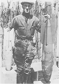 Major Andrews stands with a 25-pound fragmentation bomb and a 100-pound demolition bomb.