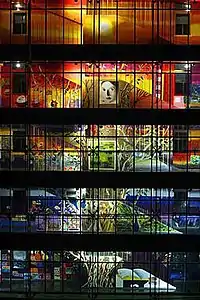 An illuminated, colorful mural painting distributed across the galleries and interior staircase along the five-floor facade of the interior courtyard of an office building