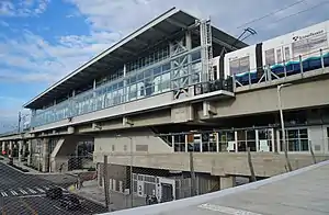 An elevated train station with glass and concrete walls, seen from a bridge jutting out from the middle of the structure.