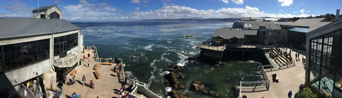 Panoramic view of the aquarium's 20,000 square feet of public decks overlooking Monterey Bay. The building's walls on either side consist mostly of windows, but there is stadium seating to the right overlooking a man-made tide pool