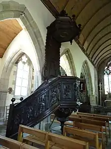 Photograph showing a carved pulpit in dark wood in the nave of a church
