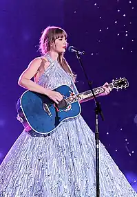 Taylor Swift wearing a midnight blue tinsel-fringed jacket singing on a mic