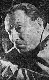 A black-and-white image of a 42-year-old man smoking a cigarette and looking to the left of the camera.